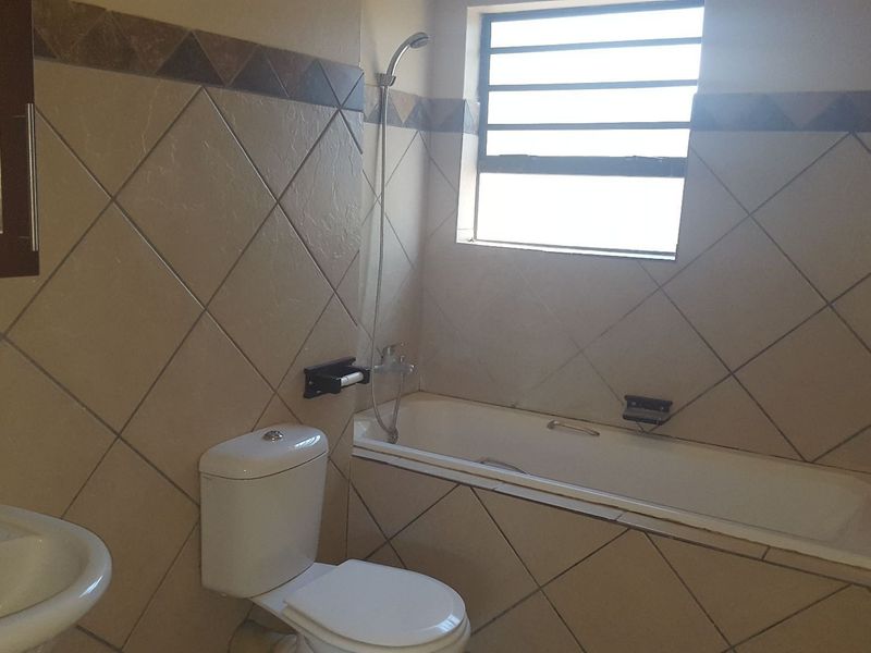 A functional bathroom featuring a bathtub with shower head, pedestal basin, and tiled walls with a louvered window for natural light.