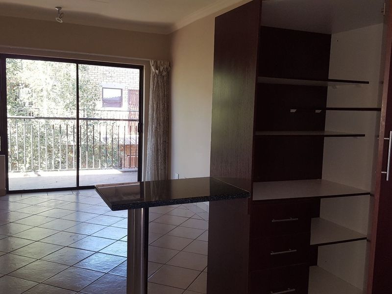 Open plan living area featuring tiled flooring, built-in cabinetry with a breakfast bar, and sliding glass doors leading to a balcony.
