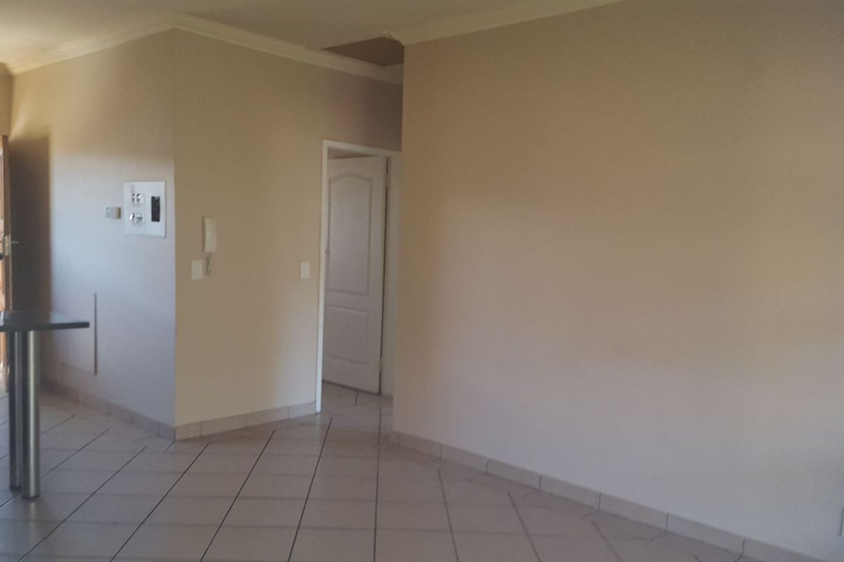 An empty, open-plan living area featuring neutral walls, tiled flooring, and an intercom system, with access to an adjacent balcony.