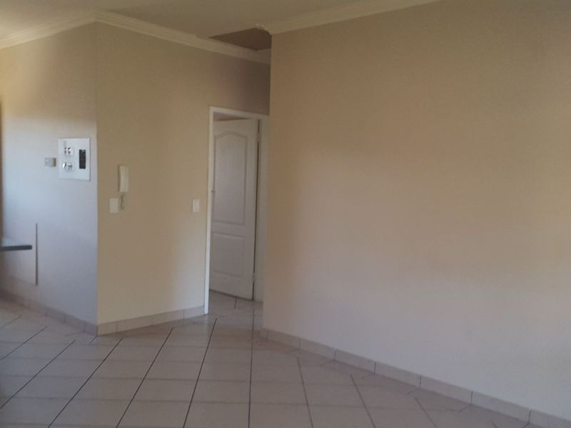 An empty, open-plan living area featuring neutral walls, tiled flooring, and an intercom system, with access to an adjacent balcony.