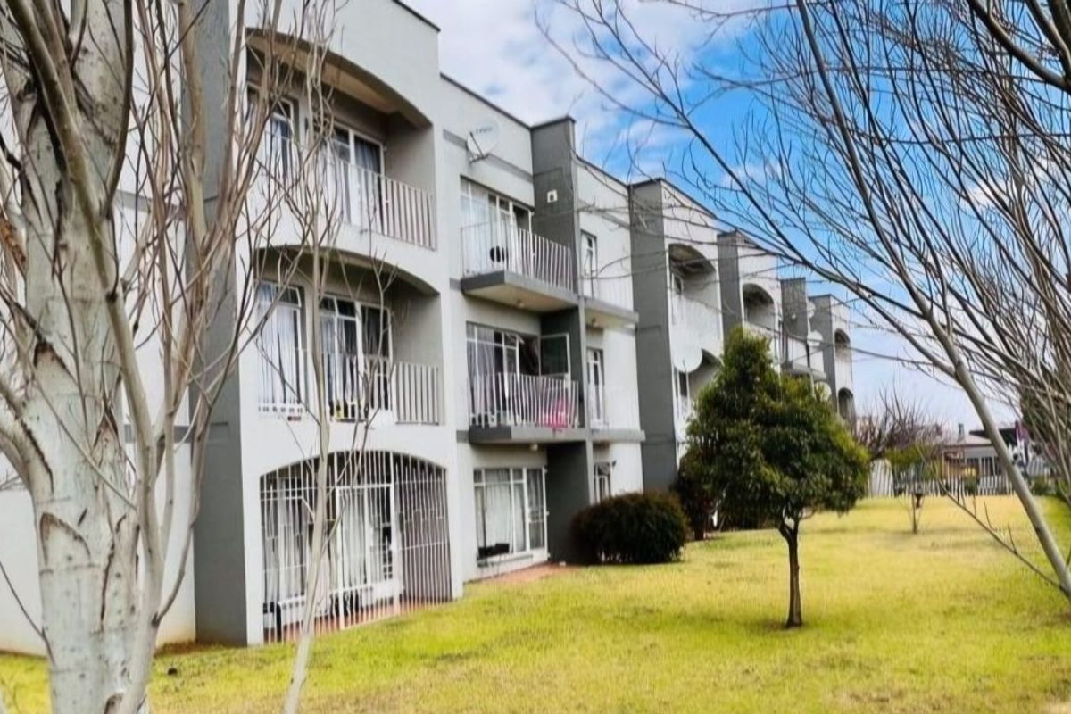 Rear view of a multi-story apartment building featuring private balconies, sliding glass doors, and security bars, set against a landscaped lawn area.
