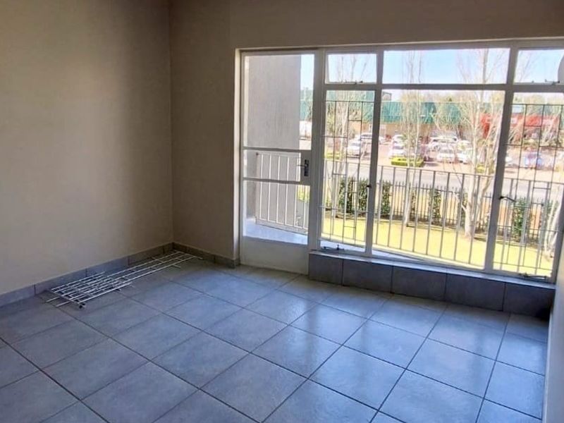An empty living room featuring tiled flooring, large windows, and a sliding door providing access to an outdoor area.