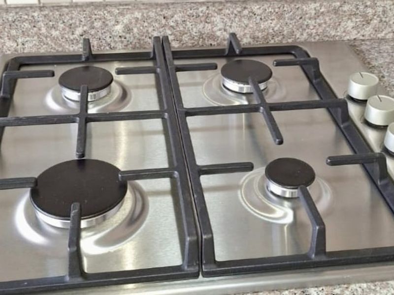 A clean, stainless steel four-burner gas hob set into a durable granite countertop with a neutral tiled backsplash.