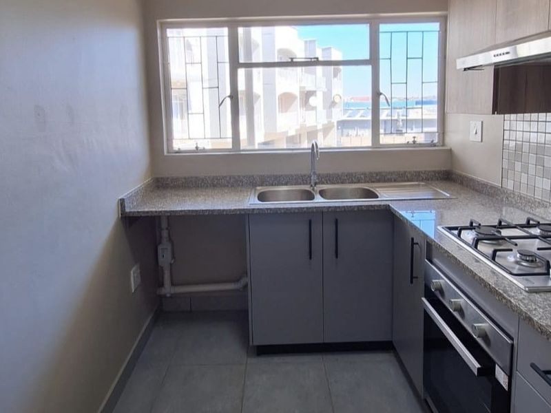 A clean, modern kitchen featuring granite countertops, built-in gas hob, oven, extractor fan, and ample cabinetry, with a window providing natural light.