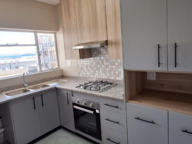 Modern kitchen featuring light grey and wood-tone cabinetry, granite countertops, a gas hob, built-in oven, and a double sink with ample natural light.