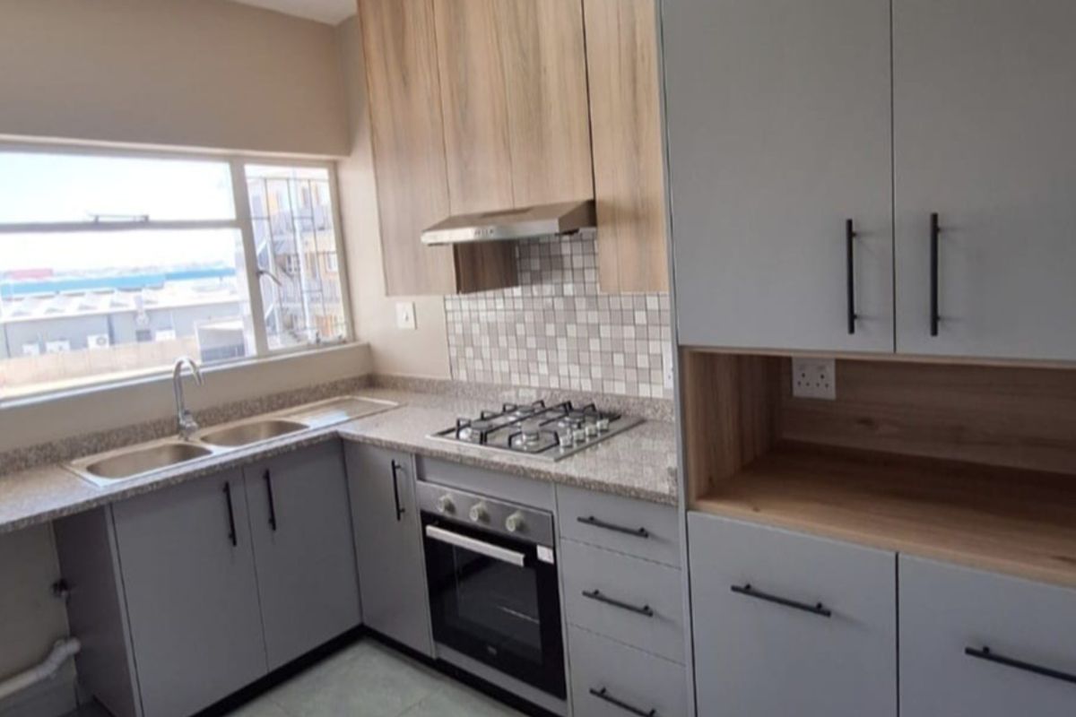 Modern kitchen featuring light grey and wood-tone cabinetry, granite countertops, a gas hob, built-in oven, and a double sink with ample natural light.