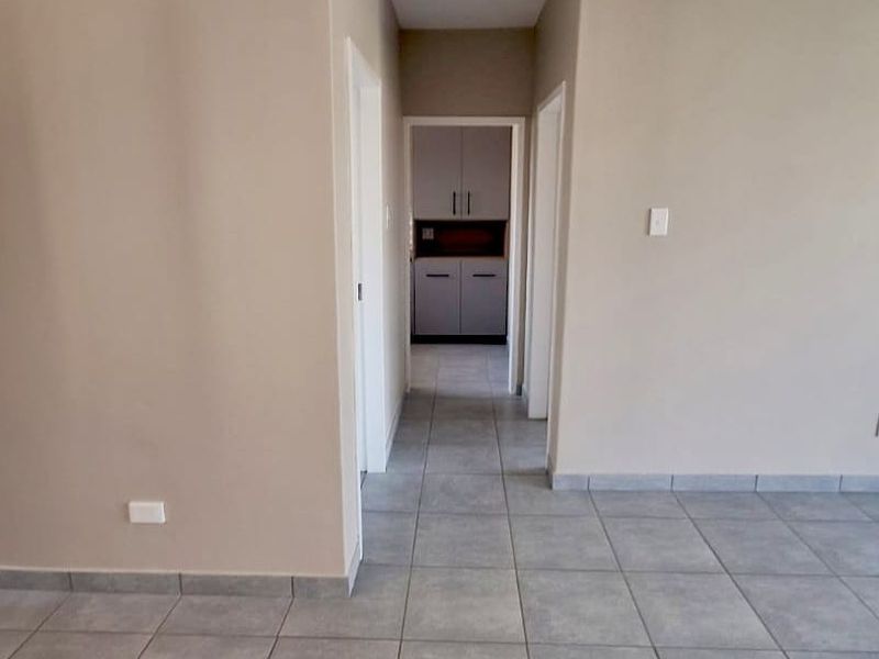 A clean, neutral-toned hallway featuring tiled flooring and skirting boards, leading towards a secondary space with built-in cabinetry.
