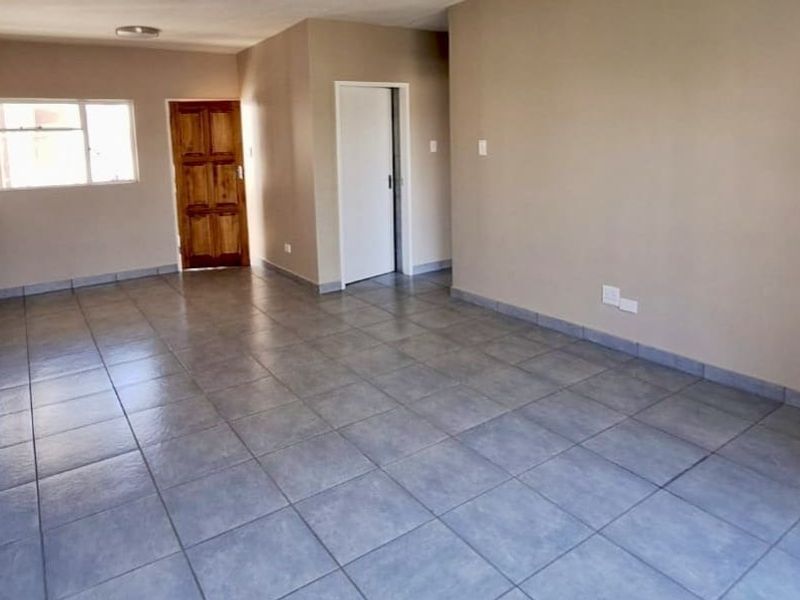 A spacious, empty living area featuring neutral wall tones and durable tiled flooring, providing a versatile blank canvas for interior design.