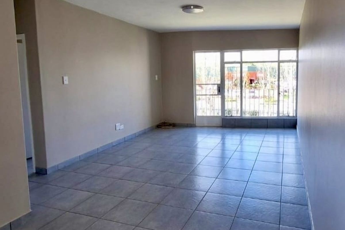 A spacious, empty living area featuring neutral walls, tiled flooring, and a large window with an integrated security gate.