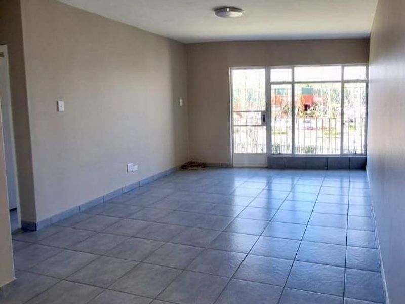 A spacious, empty living area featuring neutral walls, tiled flooring, and a large window with an integrated security gate.