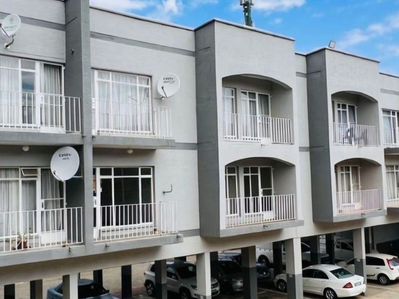 Exterior view of a multi-story apartment complex featuring private balconies with metal railings and a ground-level covered parking area.