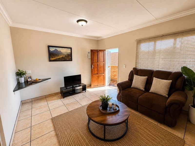 A well-maintained living room featuring tiled flooring, a built-in corner shelf, and direct access to an outdoor area through a wooden door.