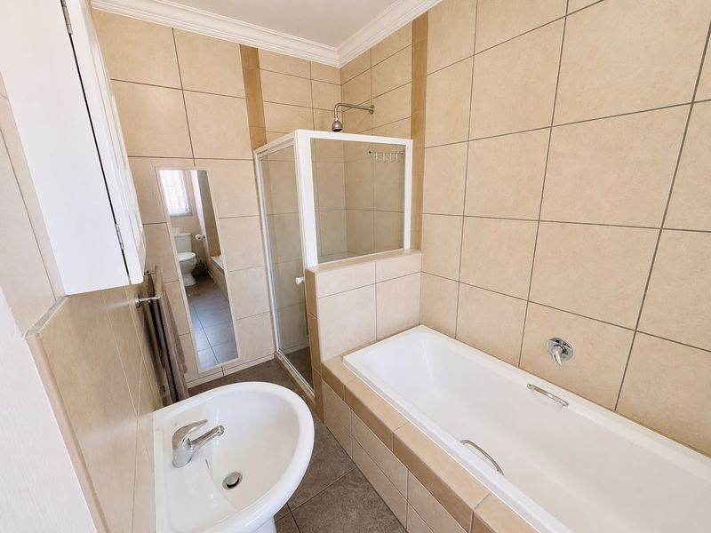 A clean, functional bathroom featuring a separate shower enclosure, a bathtub, and a pedestal basin with neutral wall and floor tiling.