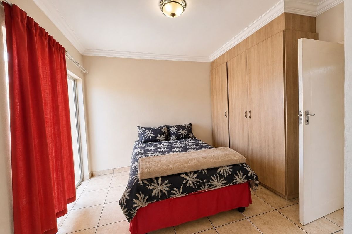 A well-maintained bedroom featuring neutral tiled flooring, built-in wooden cupboards, and a sliding glass door providing access to the exterior.