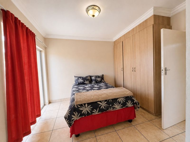 A well-maintained bedroom featuring neutral tiled flooring, built-in wooden cupboards, and a sliding glass door providing access to the exterior.