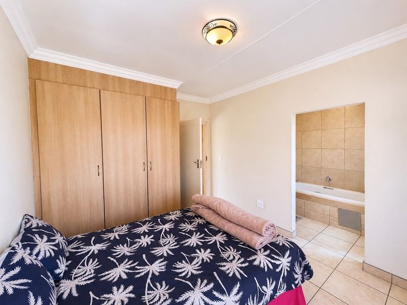 A well-maintained bedroom featuring built-in wooden wardrobes, tiled flooring, and direct access to an en-suite bathroom with a built-in bathtub.