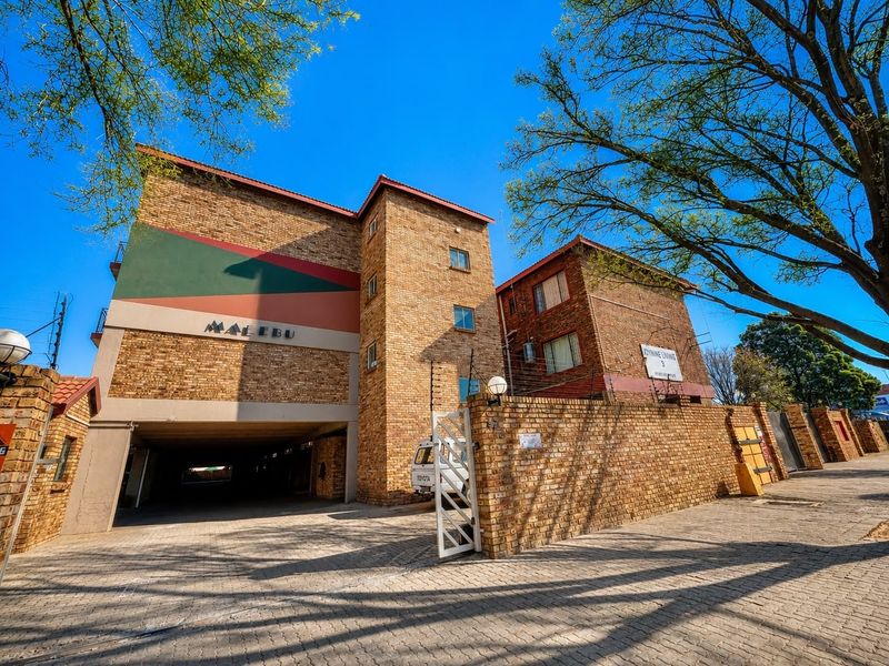 Front elevation of the Malebu apartment complex featuring face brick construction, secure gated access, and a paved driveway leading to covered parking.
