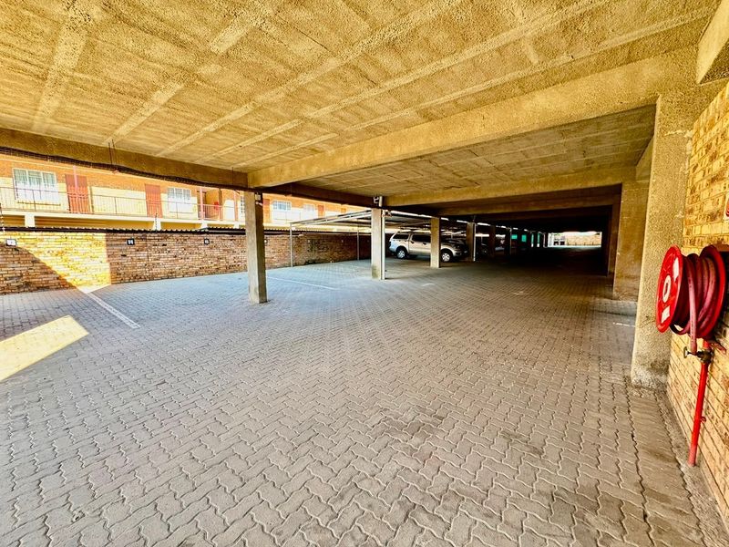 A covered parking area featuring concrete ceilings, brick walls, and paved flooring, equipped with a wall-mounted fire hose reel.