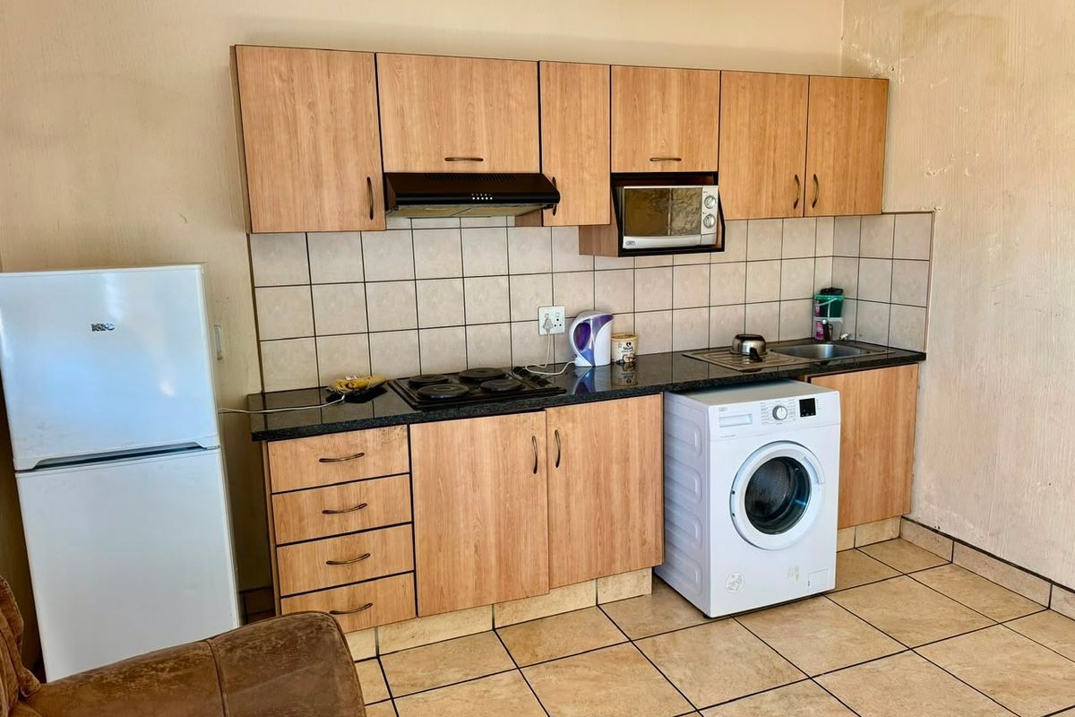 Compact kitchen featuring laminate cabinetry, stone countertops, tiled backsplash, and integrated appliances, showing signs of wall surface wear.