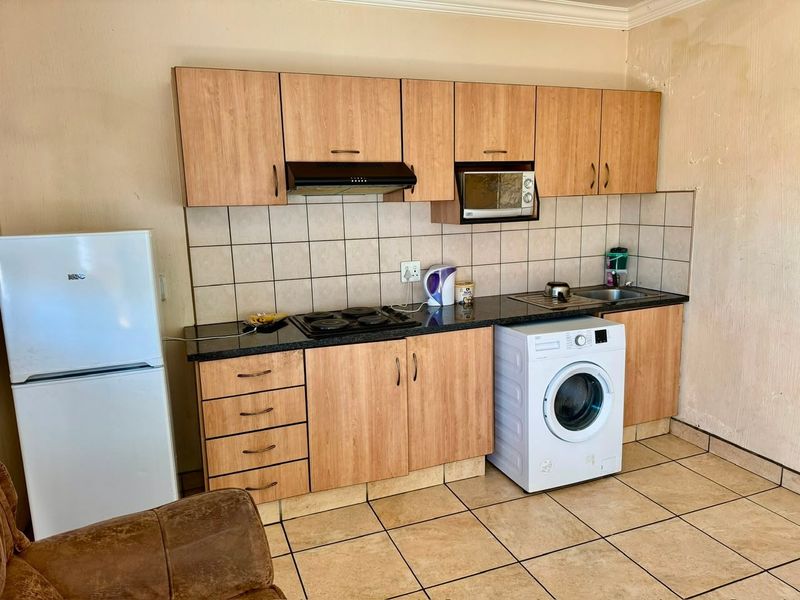 Compact kitchen featuring laminate cabinetry, stone countertops, tiled backsplash, and integrated appliances, showing signs of wall surface wear.