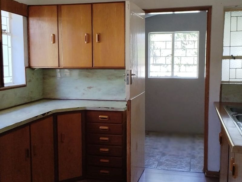 A dated kitchen featuring original laminate cabinetry, countertops, and a stainless steel sink, offering significant potential for a modern renovation.