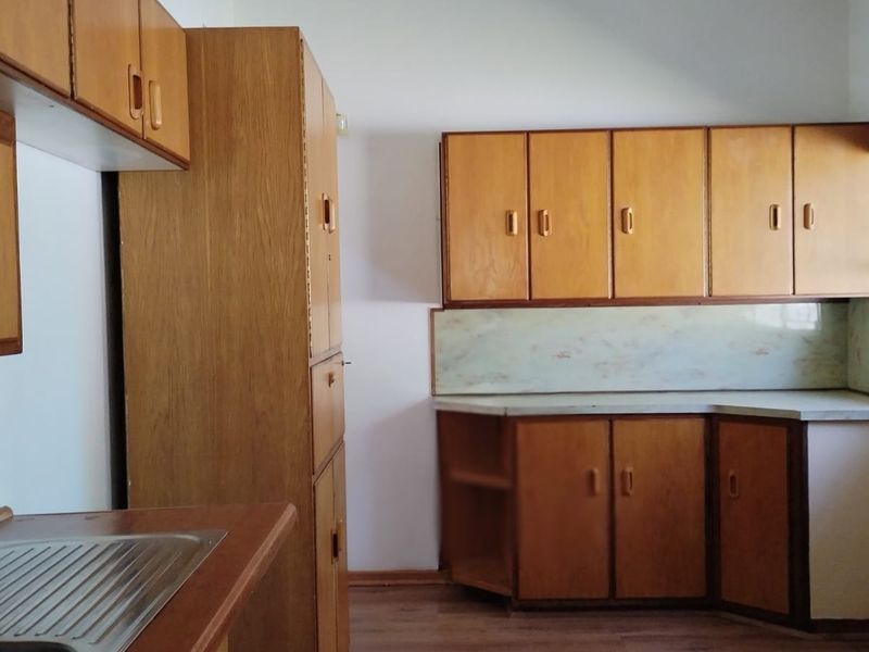 A functional kitchen featuring original wooden cabinetry, laminate countertops, and a stainless steel sink, offering a blank canvas for modern renovation.