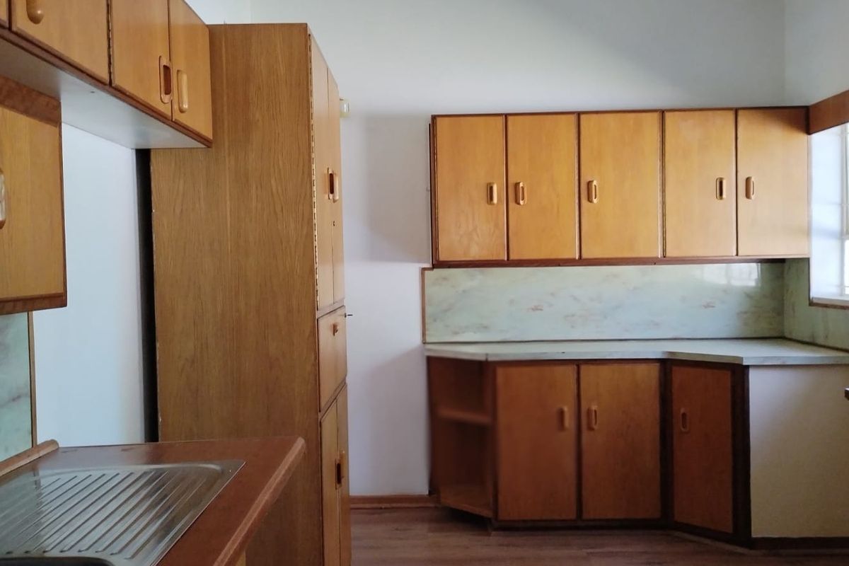 A functional kitchen featuring original wooden cabinetry, laminate countertops, and a stainless steel sink, offering a blank canvas for modern renovation.