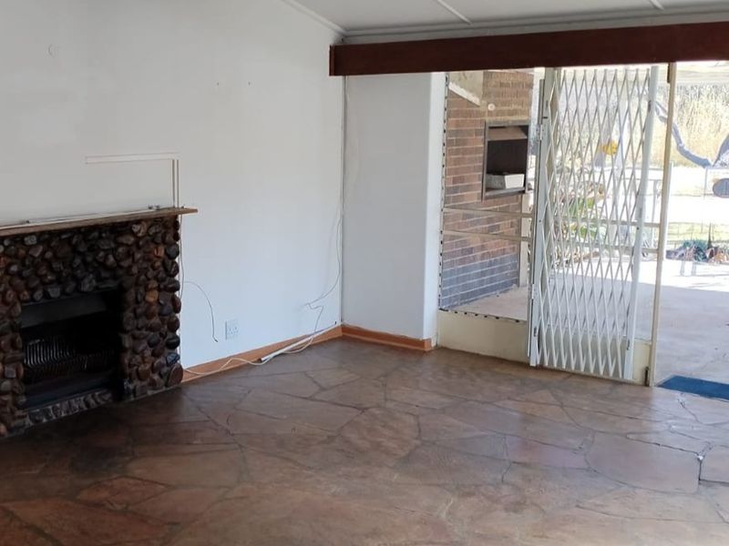 An empty living room featuring a rustic stone fireplace, flagstone flooring, and a sliding glass door leading to an outdoor area with a security gate.