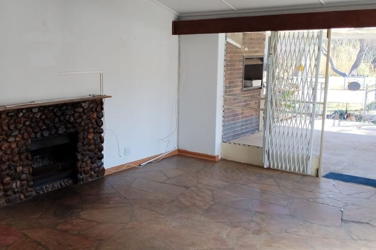 An empty living room featuring a rustic stone fireplace, flagstone flooring, and a sliding glass door leading to an outdoor area with a security gate.