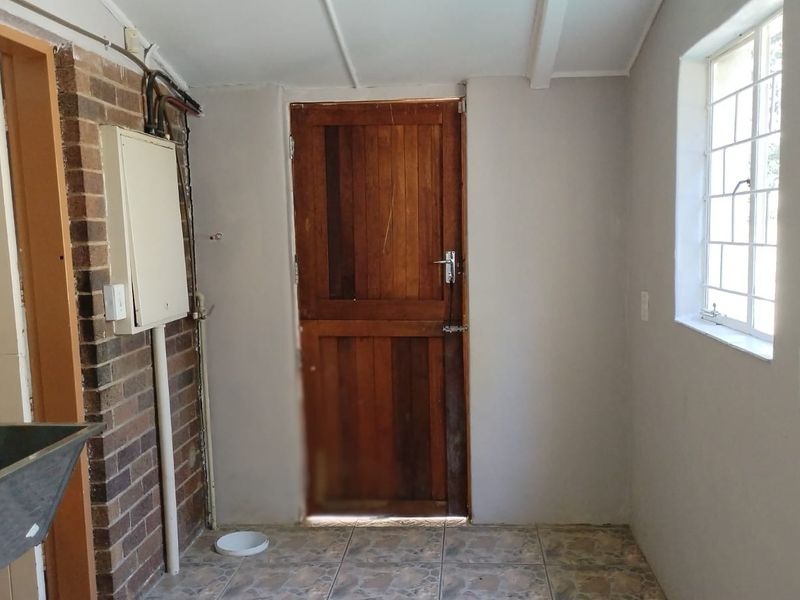 A functional laundry area featuring a stainless steel utility sink, exposed brickwork, tiled flooring, and a solid timber door leading to the exterior.