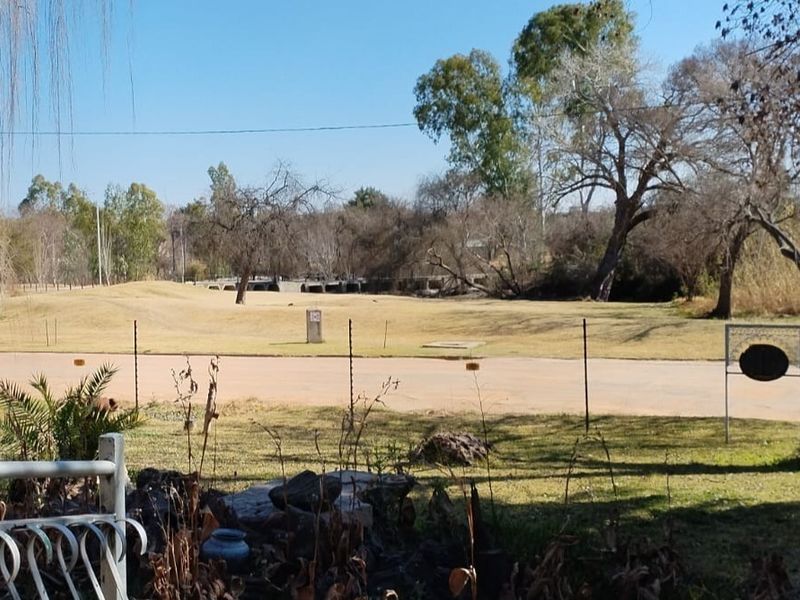 A scenic view overlooking an open field and natural landscape, featuring established trees and perimeter electric fencing.