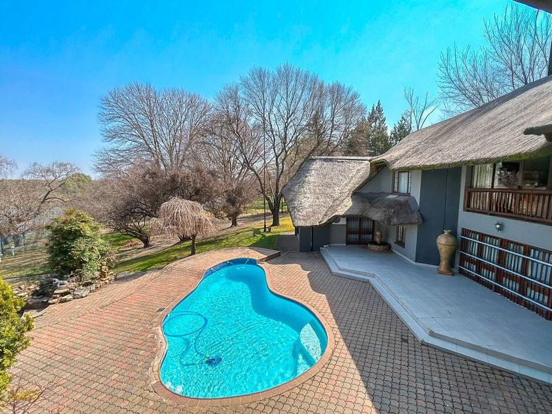 Elevated view of a swimming pool area featuring a paved patio, thatched roof architecture, and surrounding garden landscape.