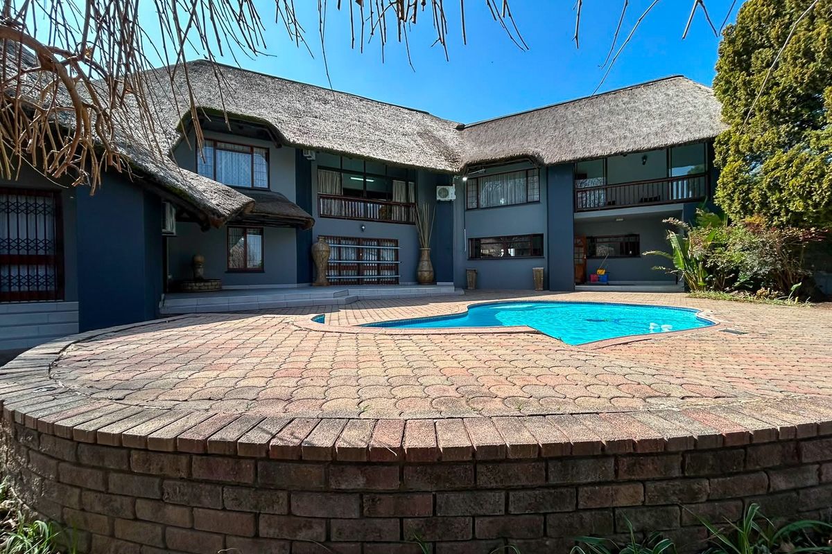 Rear view of a double-story thatched roof home featuring a swimming pool and a large brick-paved patio area.