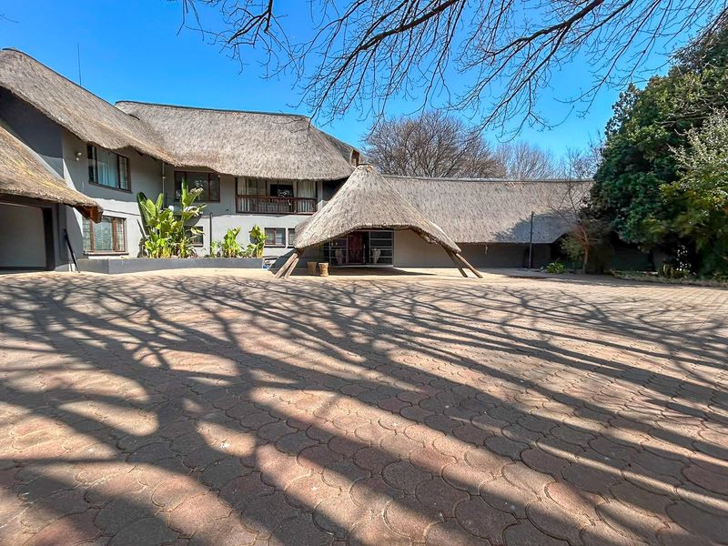 Spacious front exterior view of a large property featuring a traditional thatched roof, paved driveway, and a covered entrance area.