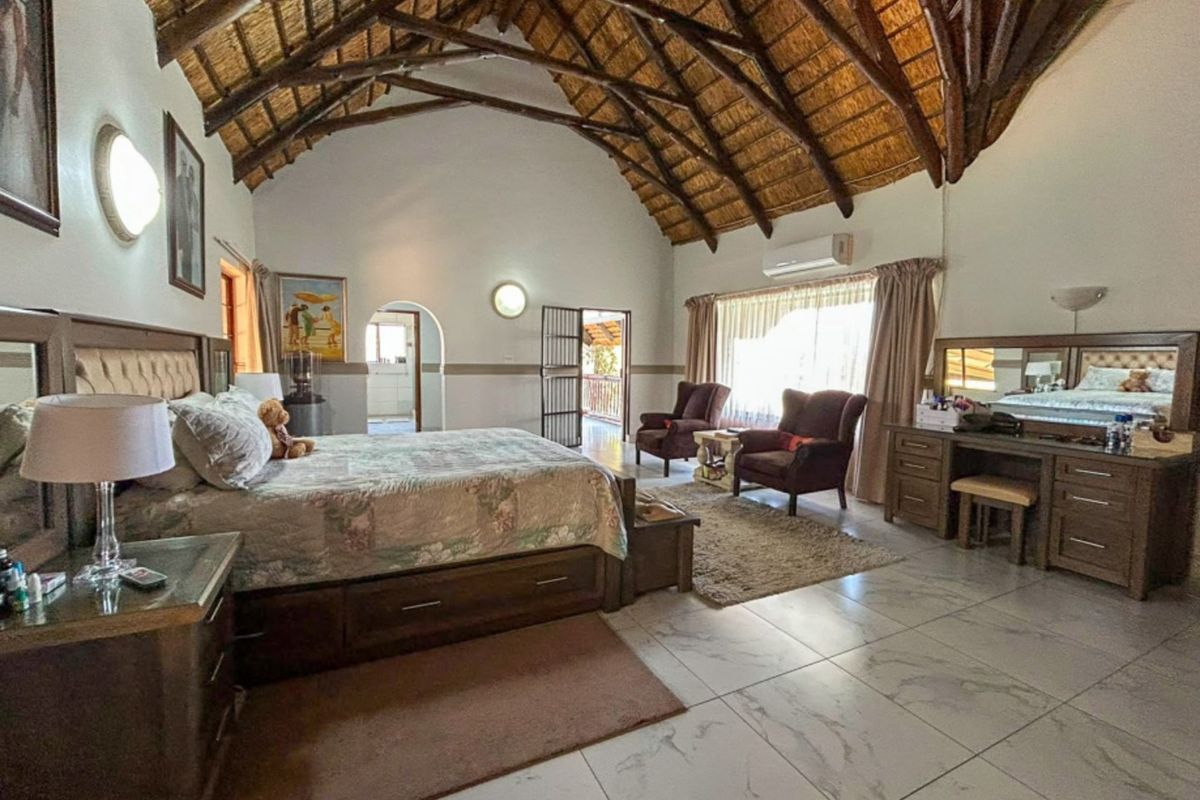 Spacious bedroom featuring a high vaulted thatched ceiling with exposed timber trusses, tiled flooring, and an integrated air conditioning unit.