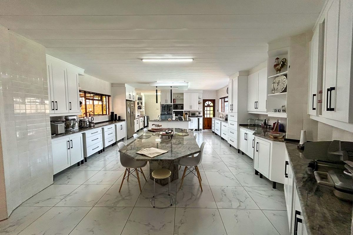 Spacious, modern kitchen featuring extensive white cabinetry, granite countertops, a large central island, and marble-look tiled flooring.