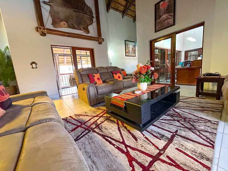 Spacious living room featuring a high thatched ceiling with exposed timber beams, tiled flooring, and large sliding glass doors leading to an outdoor area.