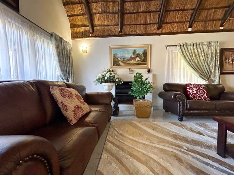 A cozy living room featuring a traditional thatched roof with exposed timber rafters, tiled flooring, and a central fireplace.
