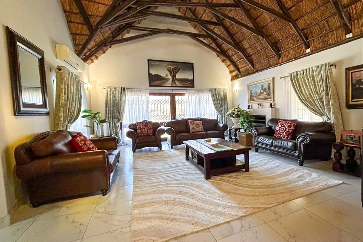 Spacious living room featuring a high vaulted thatched ceiling with exposed timber trusses, tiled flooring, and a fireplace, creating a warm and inviting atmosphere.