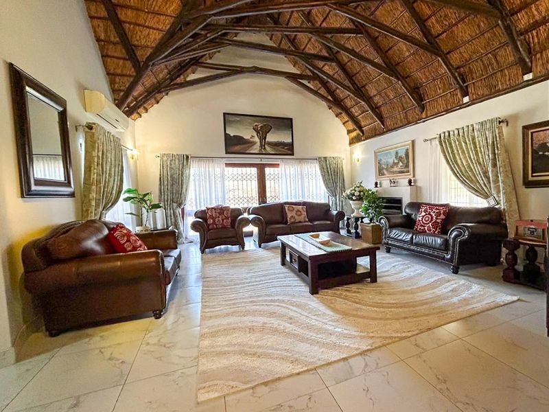 Spacious living room featuring a high vaulted thatched ceiling with exposed timber trusses, tiled flooring, and a fireplace, creating a warm and inviting atmosphere.
