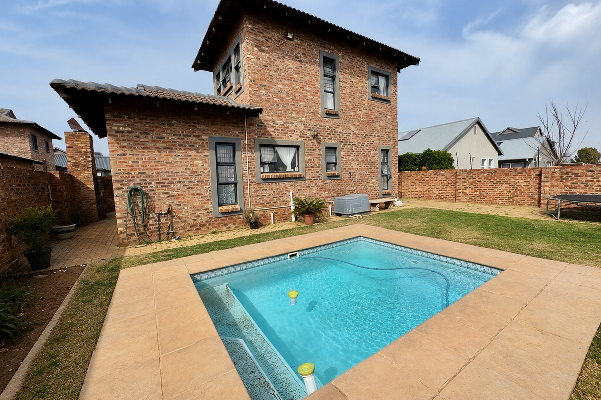 Rear view of a double-story face-brick house featuring a private swimming pool with paved surround and a landscaped garden area.