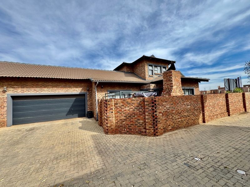 A well-maintained face brick house featuring a tiled roof, a double garage, and a paved driveway with a secure brick boundary wall.