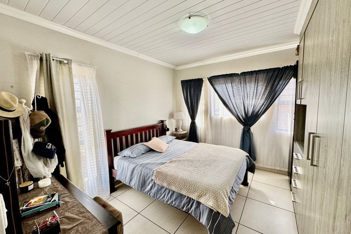 A functional bedroom featuring tiled flooring, built-in cupboards, and a tongue and groove ceiling, offering a clean and practical living space.
