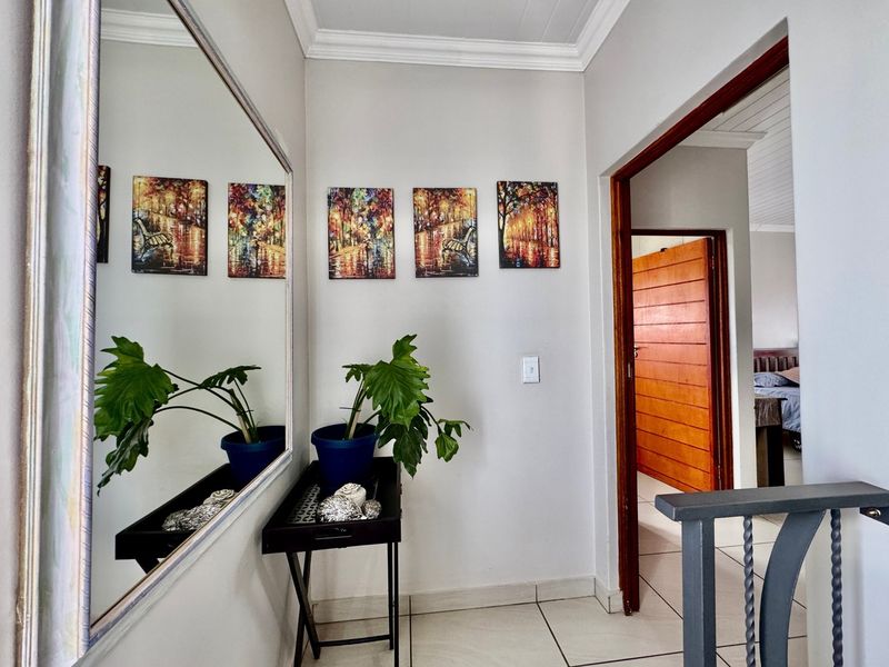 A well-maintained hallway featuring tiled flooring, crown molding, and a clear view into an adjacent bedroom through a wooden door frame.