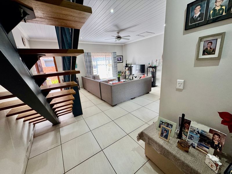 Open-plan living area featuring a modern timber staircase with steel frame, tiled flooring, and a tongue and groove ceiling with integrated lighting.