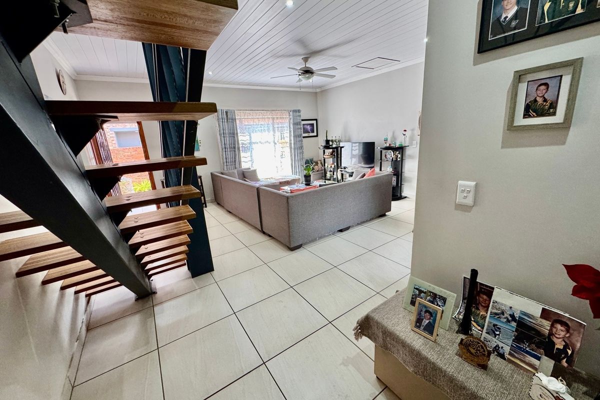 Open-plan living area featuring a modern timber staircase with steel frame, tiled flooring, and a tongue and groove ceiling with integrated lighting.