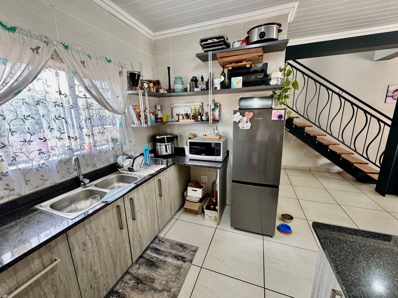 A functional kitchen featuring granite countertops, laminate cabinetry, open shelving, and tiled flooring, adjacent to an open staircase with a decorative metal railing.