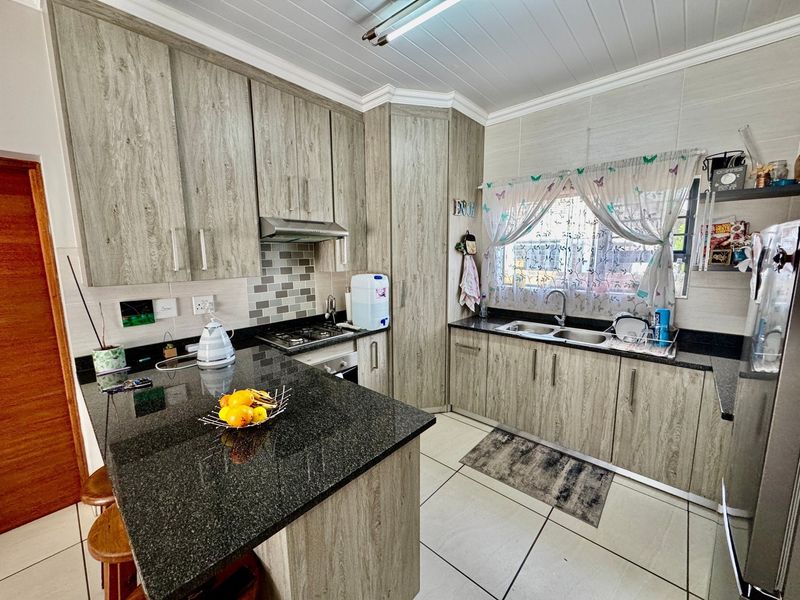 A functional kitchen featuring wood-look laminate cabinetry, dark granite countertops, a gas hob with extractor, and tiled flooring throughout.