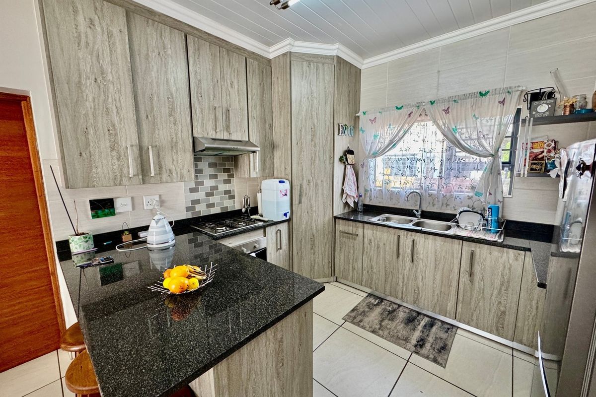 A functional kitchen featuring wood-look laminate cabinetry, dark granite countertops, a gas hob with extractor, and tiled flooring throughout.