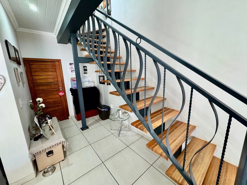 A bright hallway featuring a modern staircase with wooden treads and a decorative wrought iron balustrade, complemented by neutral tiled flooring.